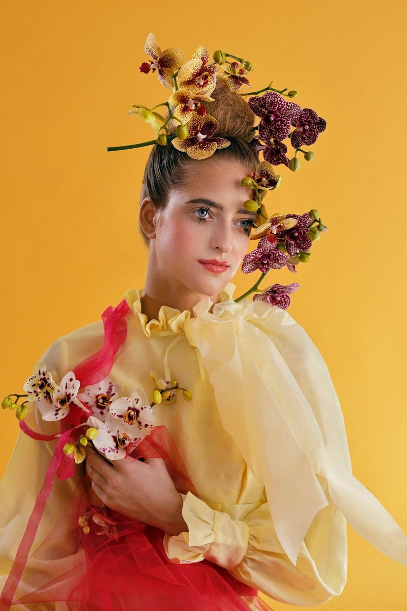 A model stands in front of a yellow background wearing a floral headdress in this portrait taken by Guia Besana with a Canon RF 50mm F1.2L USM lens. 