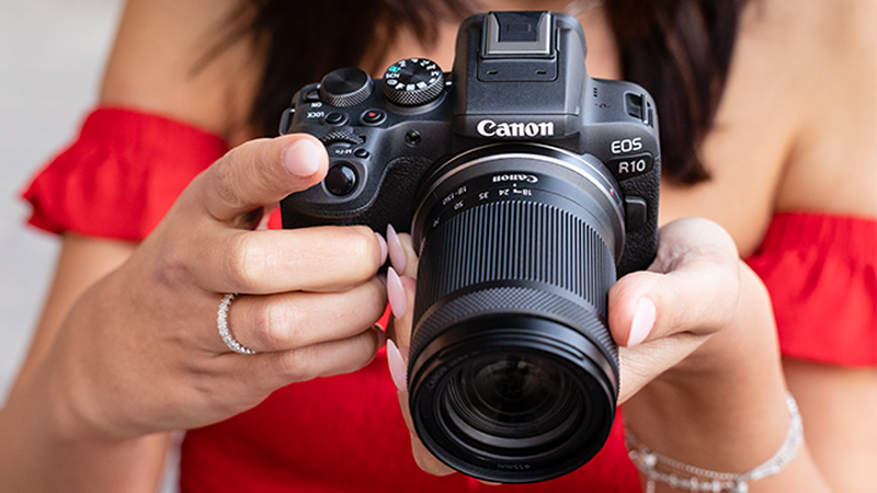 A woman in a red dress holding EOS R10 in her hands.
