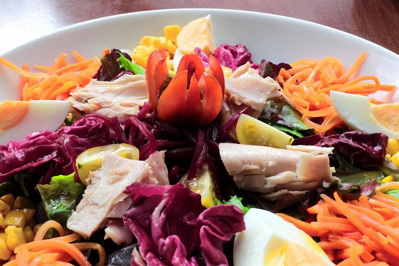 A close-up of a salad bowl filled with shredded carrots, boiled egg quarters, sliced red cabbage, mushrooms and sweetcorn.