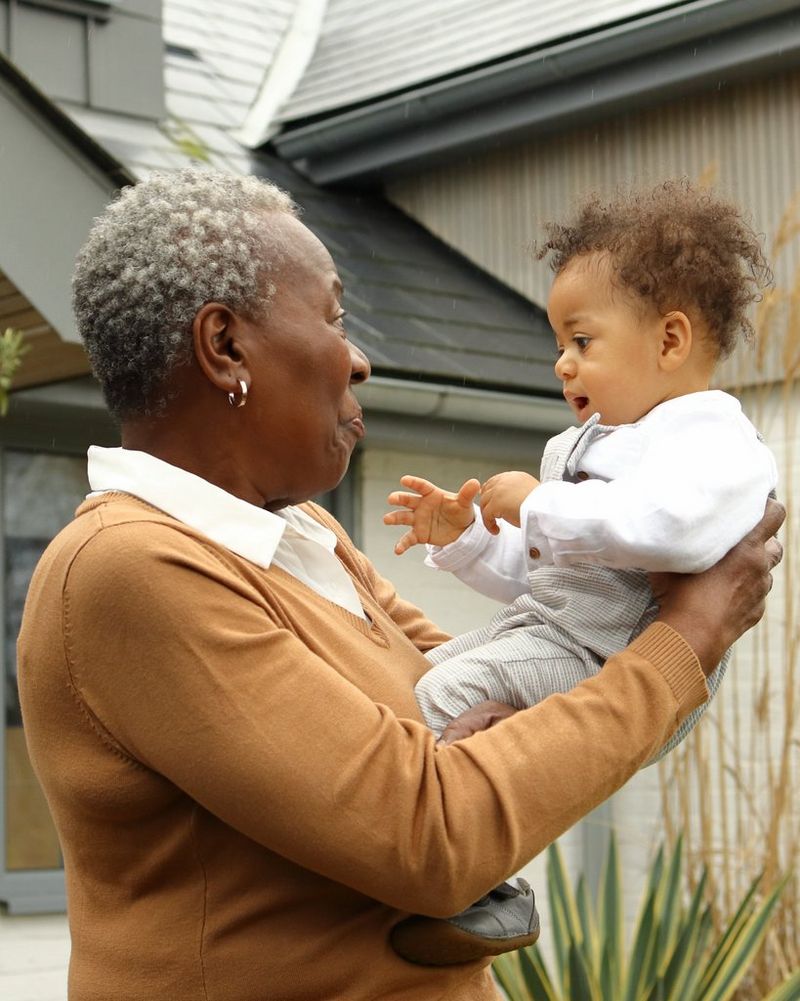 A grandmother holding her grandchild in her arms and talking to them. 