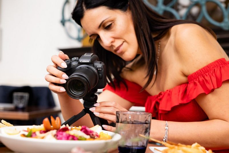 A woman photographing a plate of food with a Canon EOS R10 on a tripod.