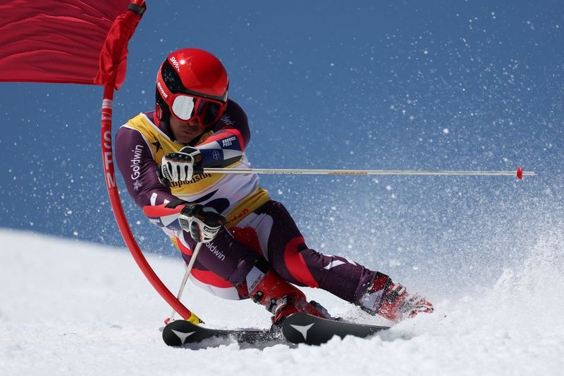 A skier captured in motion manoeuvring around a red flag, kicking up snow. Taken on a Canon EOS R3 with a Canon RF 100-500mm F4.5-7.1L IS USM lens.