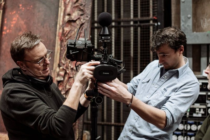 Clive Booth and Tom Rogers stand on either side of a Canon EOS R5 C with a Canon RF 5.2mm F2.8L DUAL FISHEYE lens and make adjustments to the setup. 