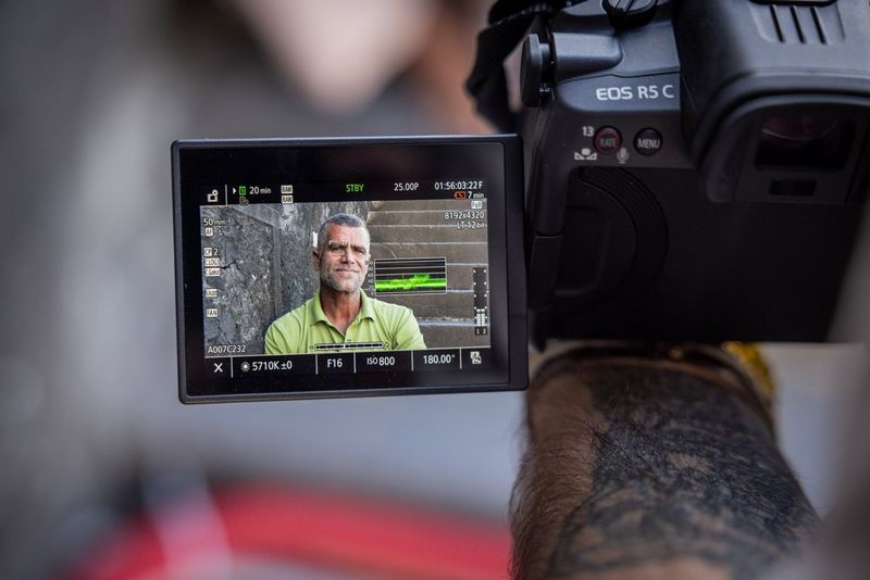 A Canon EOS R5 C camera with the rear screen showing a man in a green t-shirt, as well as various selected camera settings.