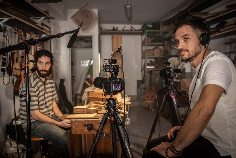 A Canon EOS R5 C and Canon EOS C70 on tripods in a craft workshop. Next to them, two seated men are looking at something to the left of the camera.