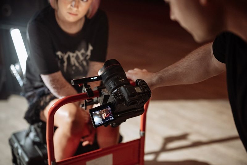 A photographer looking at a Canon EOS R5 Mark II camera’s screen which is filming a girl sat down. 