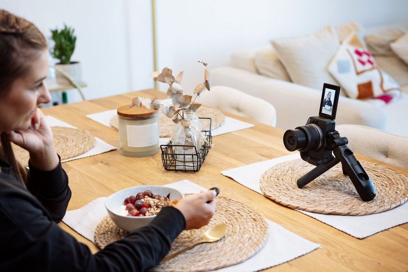 Lifestyle and fitness influencer Elena Bulkowski sits at a table eating a bowl of cereal, with a Canon EOS R50 on a tripod grip in front of her, the touchscreen flipped up.