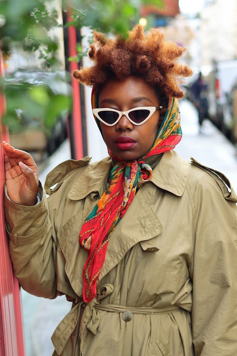 A portrait taken on a Canon EOS R50 of content creator Fatou N'Diaye in a trench coat, colourful scarf and triangular sunglasses.