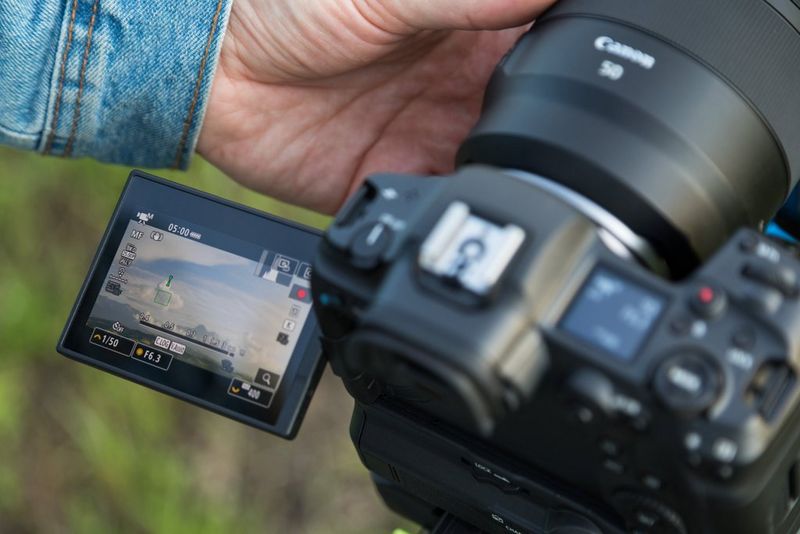 A close-up of the LCD screen of a Canon EOS R5 camera, which a person is using to film a mountain setting.