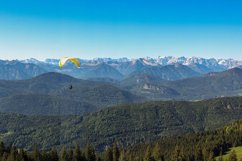 A paraglider with a yellow canopy high above the lush German Alps.