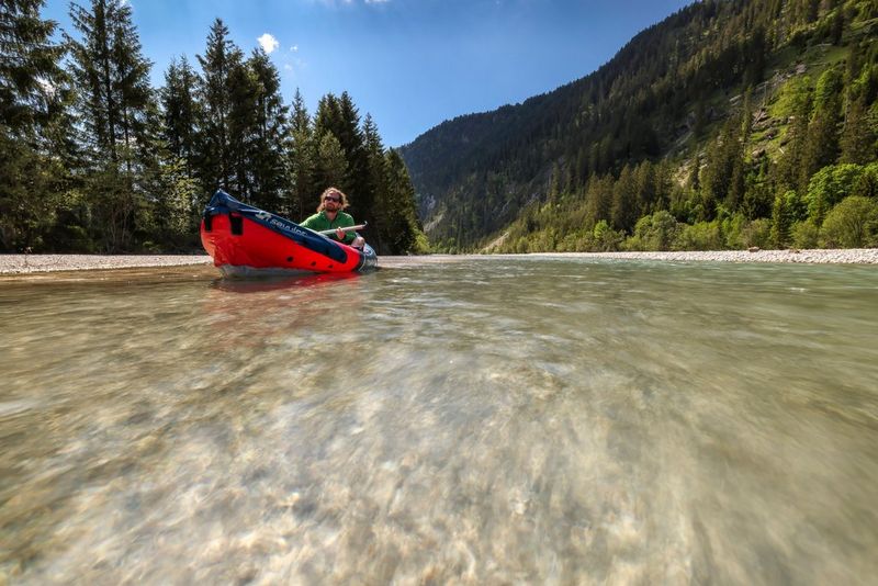 A man rowing a red canoe down a river surrounded by trees.