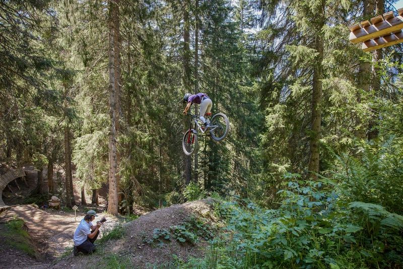 Sports photographer Teddy Morellec crouches on the forest floor, pointing his Canon EOS R6 Mark II up towards a mountain biker who has just launched themselves off a ramp.