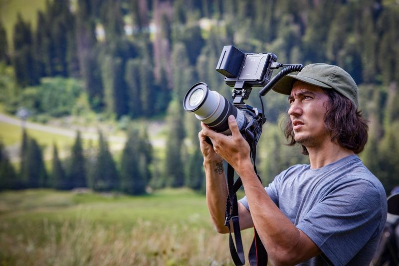 Sports photographer Teddy Morellec stands in front of tree-covered mountains filming with a Canon EOS R6 Mark II.