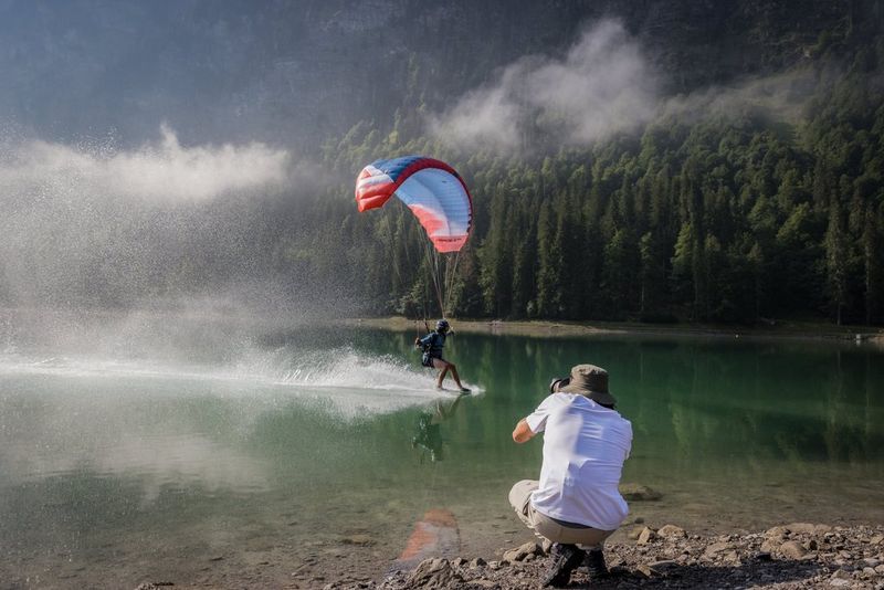 Sports photographer Teddy Morellec crouches by the side of a lake with a Canon EOS R6 Mark II to photograph a speed flyer skimming the water's surface.