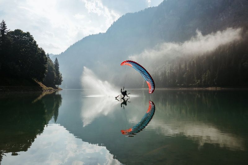 An image, taken on a Canon EOS R6 Mark II, of a speed flyer splash landing in a lake, their reflection visible on the surface of the water.