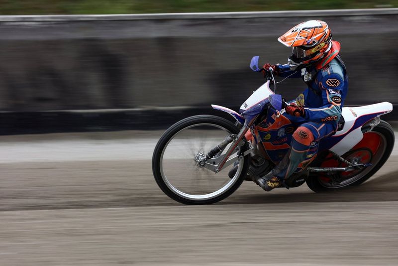 A motorbike being ridden on a speedway track with the background blurred by the camera panning.