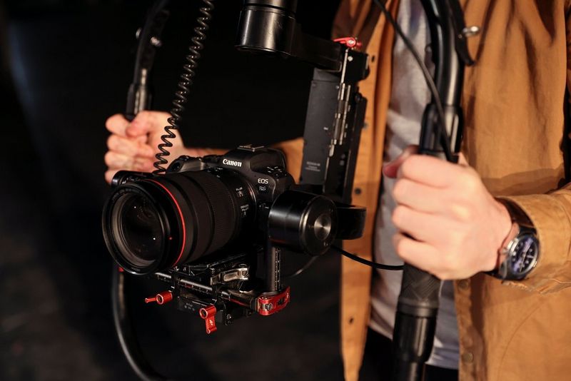 A Canon EOS R6 being used for filming in a gimbal held by a man’s hands on each side.