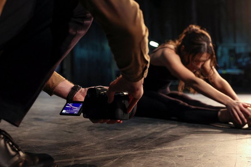 A photographer holds an EOS R6 close to floor level, taking advantage of the Vari-angle screen to photograph a dancer stretching.