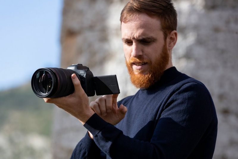 A bearded man looking at the vari-angle touchscreen on a Canon camera. 