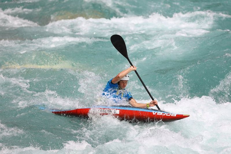 A canoeist twists their way through white water, their oar raised in the air on one side.