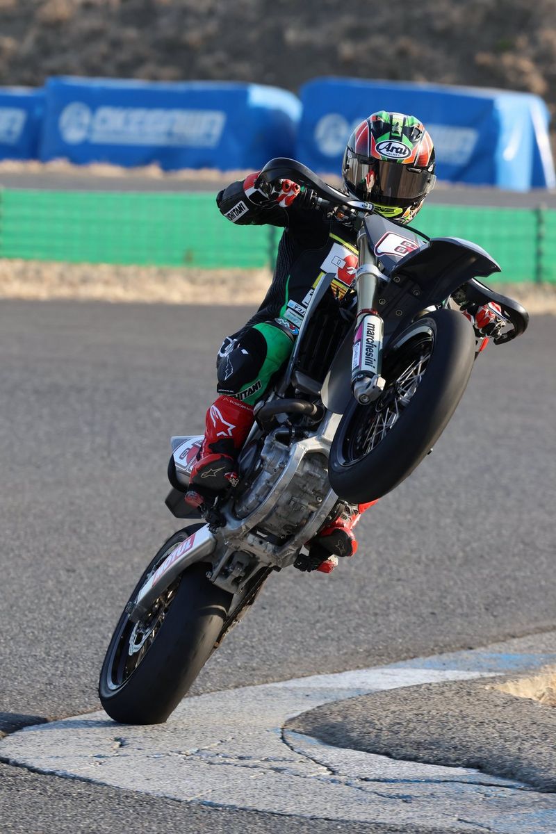 A motorbike rider performing a wheelie on a curve on a racetrack, photographed using a Canon EOS R7.