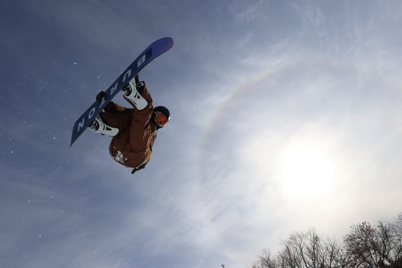 A snowboarder leaps through the air, the sun hazy in the sky alongside.