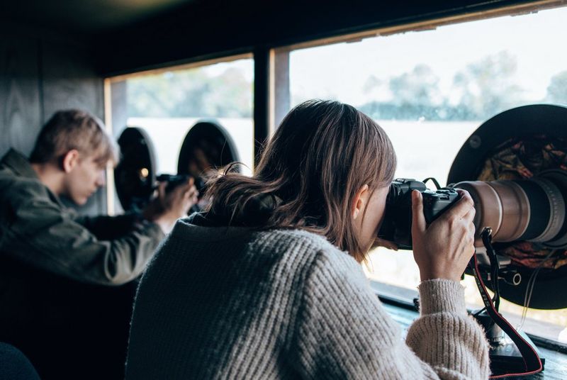 Two photographers sitting side-by-side in a bird hide.
