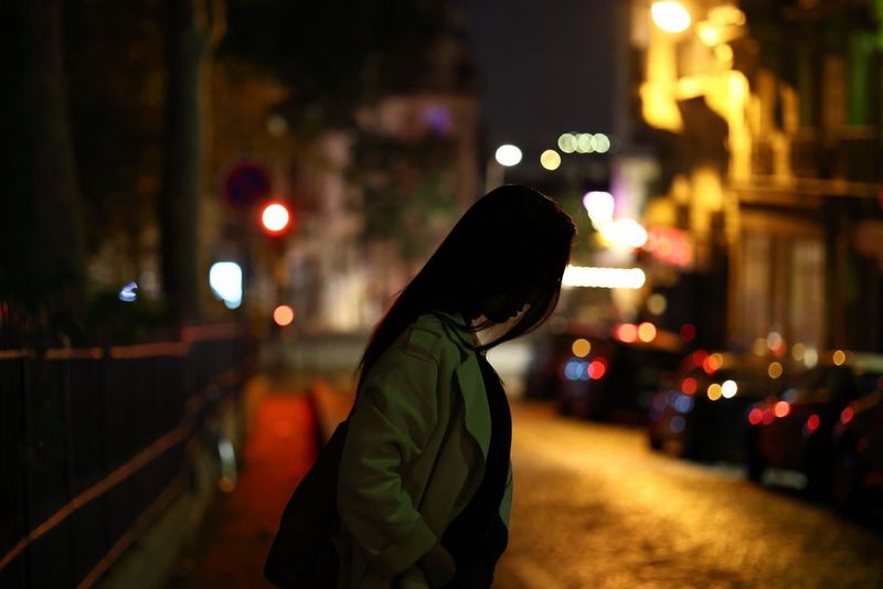 A woman crosses a road at night, with cars and a traffic signal visible in the background. 