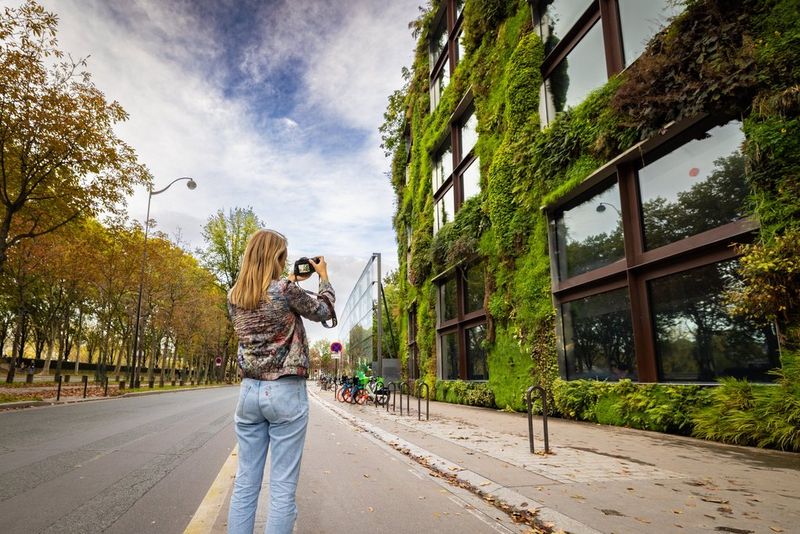 Photographer Alexandra Andreeva stands on a Paris street photographing an ivy-covered building with a Canon EOS R8.  