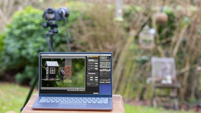 A laptop sits on a table outdoors near a camera on a tripod, with the screen showing the image feed from the camera plus settings at the side.