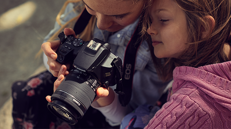 A mother and a daughter looking at the LCD screen of a camera.