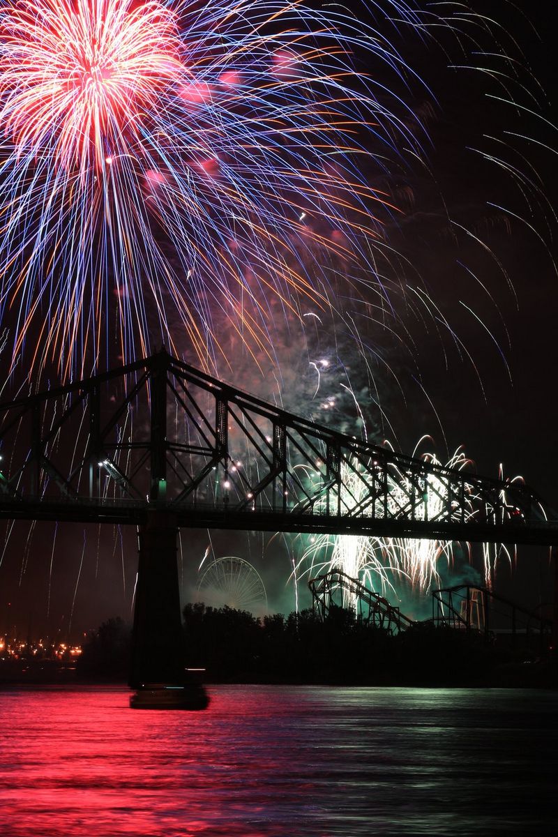 Pink and purple fireworks light up the sky above a bridge. 