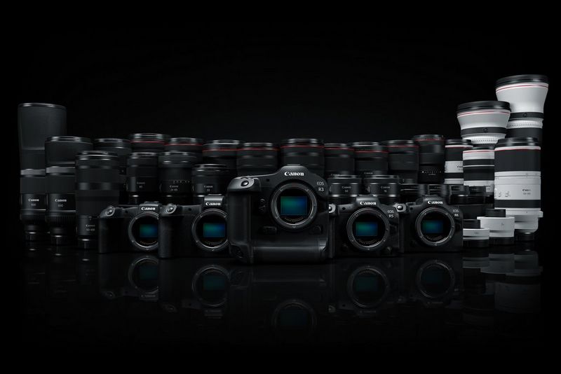 A row of Canon EOS R System cameras displayed in front of a row of RF lenses. 