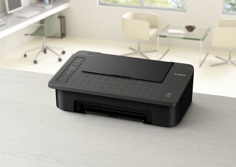 A Canon PIXMA printer on the edge of a table. Various desks and chairs can be seen in the background.