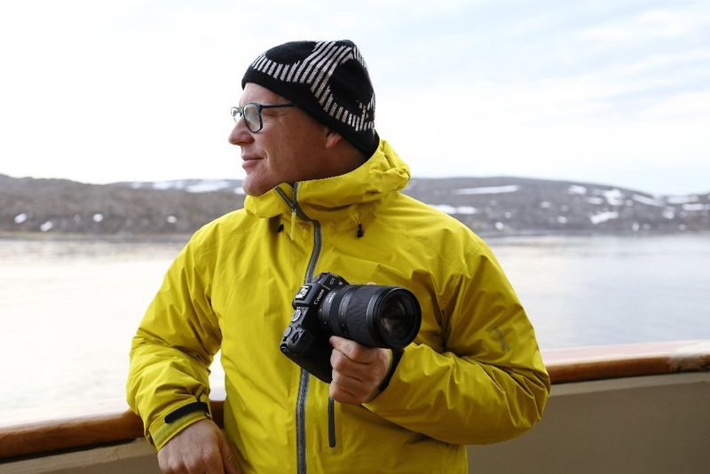 Richard Walch stands holding a Canon camera with RF 24-240mm F4-6.3 IS USM lens and looking out at a snowy seashore.