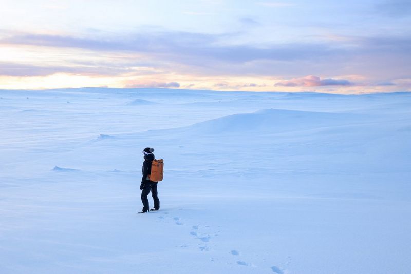 A woman carrying an orange backpack walks across a snow-covered landscape.