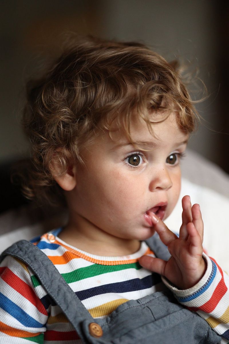 A toddler deep in thought looking into the distance with their finger seemingly touching their brand new tooth.