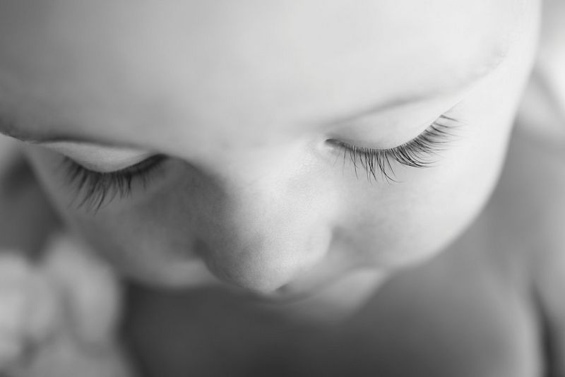 A top-down picture in black and white showing the baby’s face with their eyes closed and long eyelashes in focus.