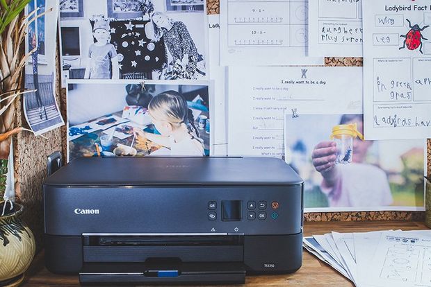 A Canon PIXMA TS5350 Series printer on a desk in front of a pinboard covered in printouts.