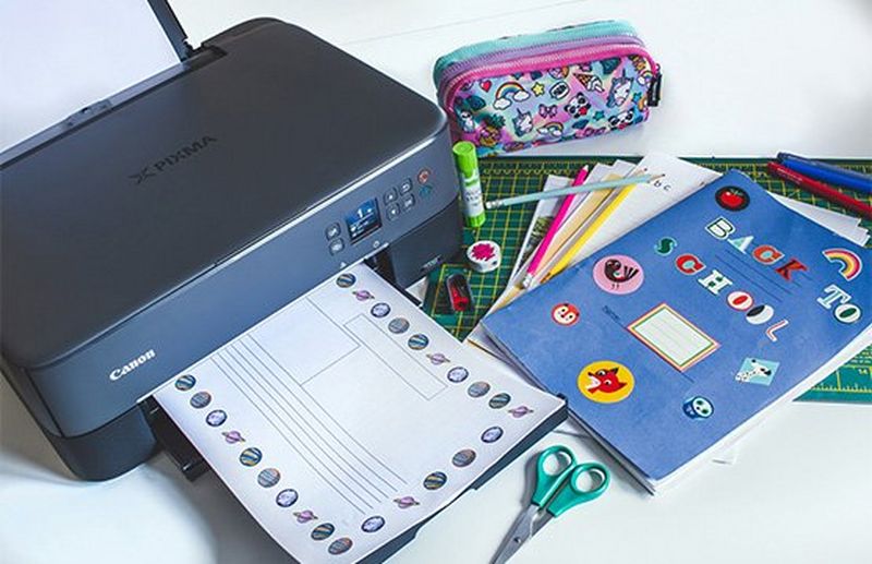 A Canon PIXMA TS5350 Series printer next to school books, a pencil case and a pair of scissors.