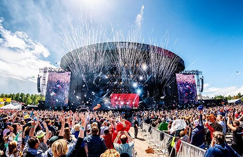 A crowd of people watch music on a huge festival stage in the sun. Photo by Bart Heemskerk.