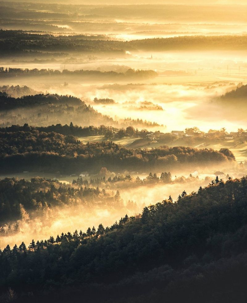Mist fills the valleys between tree-covered mountains. The contrast has been boosted and a warm tint added to increase the autumnal feeling.