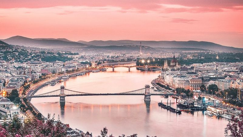 A view over the Danube towards Gellérthegy in Budapest, Hungary, taken from an elevated position, with a warm red-orange tint.