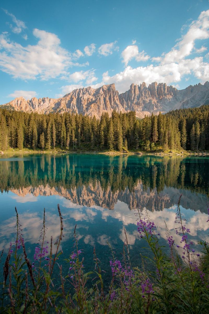 Lago di Carezza in South Tyrol, Italy, on a bright summer day, with the Dolomite Mountains in the background reflected in the still water of the lake. 