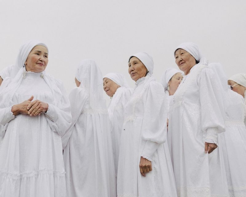 A group of older women, all immaculately dressed in matching white robes and headscarves, taken from below.