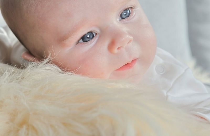 A close-cropped photo taken on a Canon EOS R10 of a baby raising its head from a fluffy blanket and looking intently to one side.