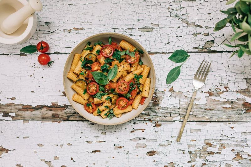 A bowl of tomato and basil pasta shot top down with a fork, basil leaves and pestle and mortar in frame, taken on a Canon EOS RP with a Canon RF 35mm F1.8 MACRO IS STM lens.