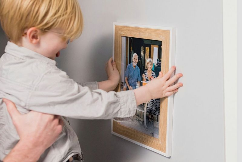 A young boy helping to hang a framed picture of his grandparents on a wall.
