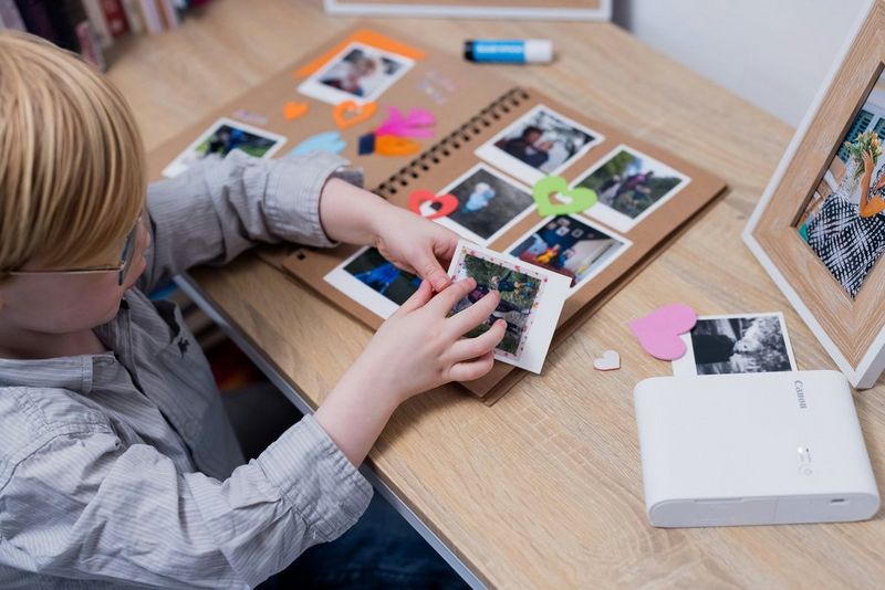 A young boy sticking printed photos into a brown paper scrapbook.