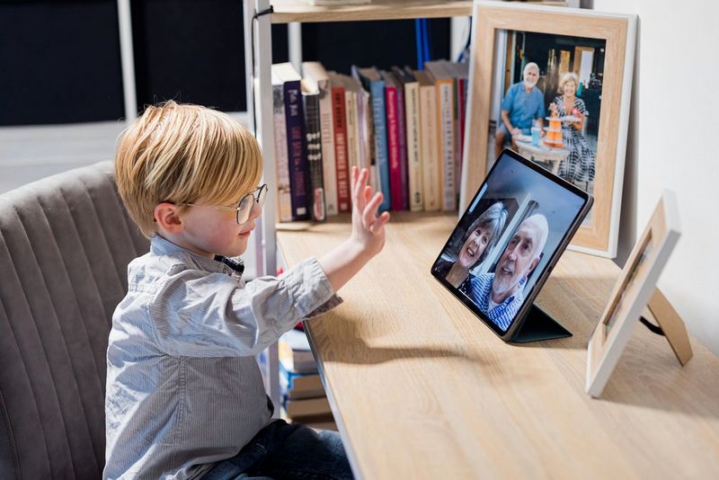A young child waving at his grandparents during a video call on a tablet.